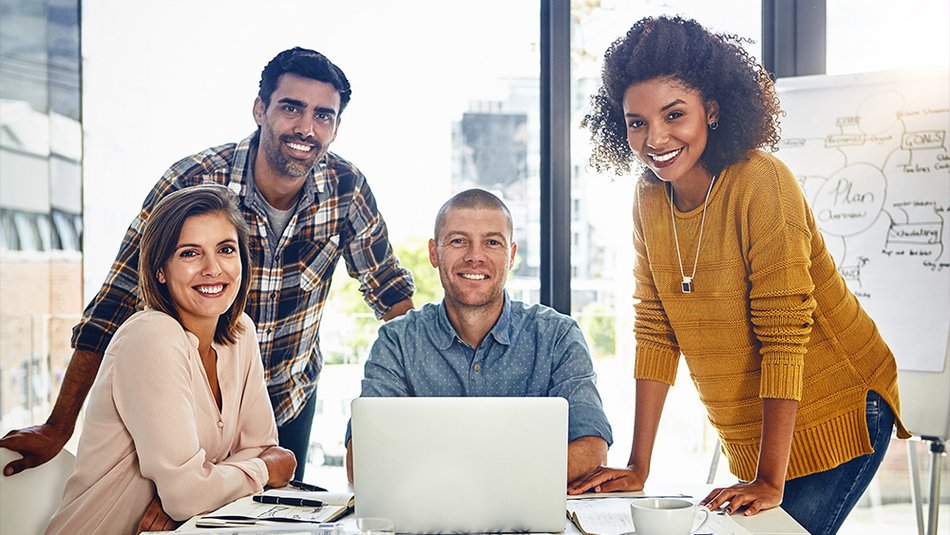 4 people surrounding the computer and smiling at the camera