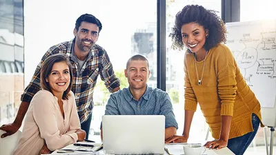 4 people surrounding the computer and smiling at the camera