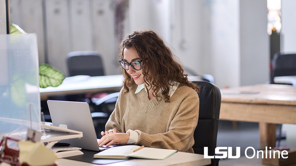 A woman smiles while working at a laptop computer.