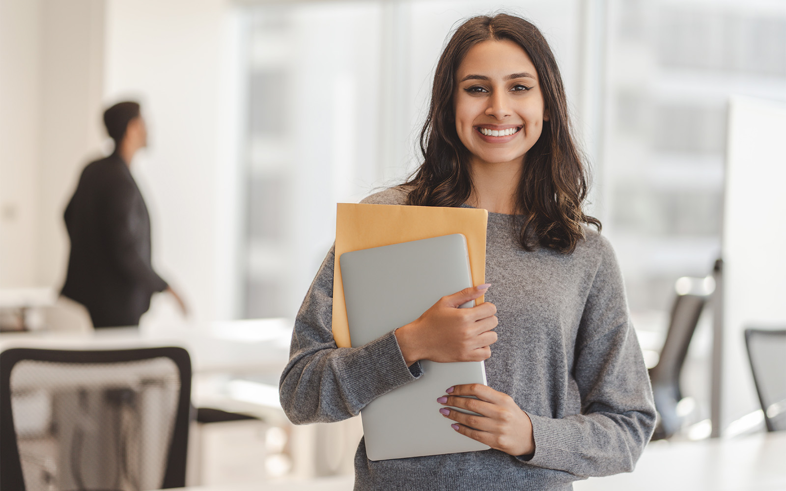 man in button up shirt standing in an open office smiling at the camera