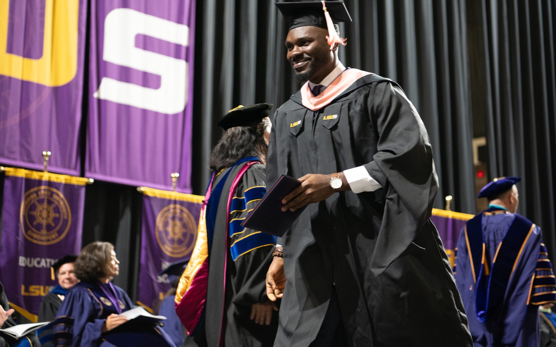African American male walking graduation stage in masters gown.