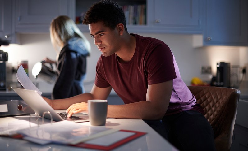 Man sitting at his kitchen counter drinking coffee and studying on his laptop.