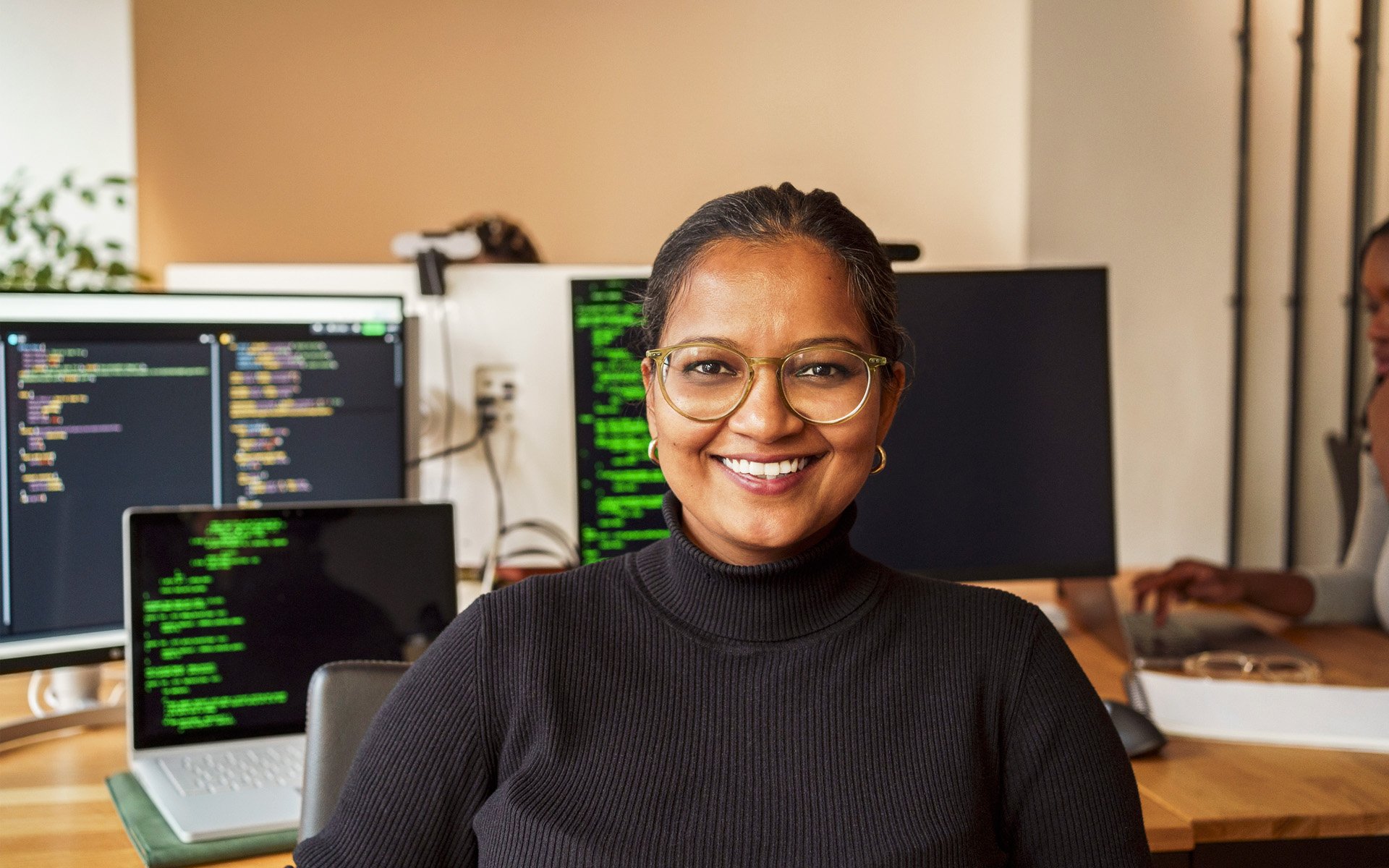 Portrait of smiling female software engineer sitting in front of desk.