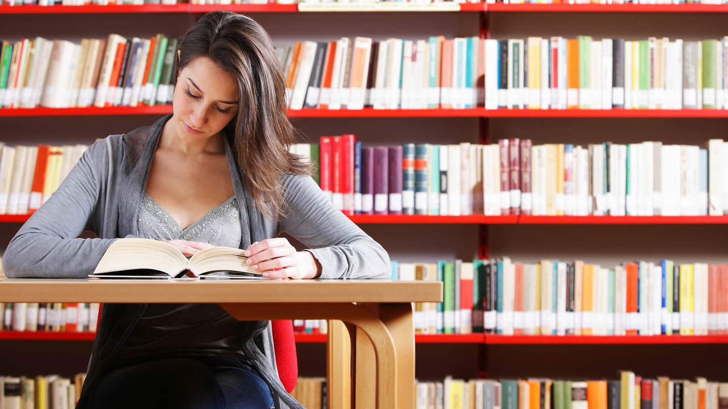 English student reading textbook in library.