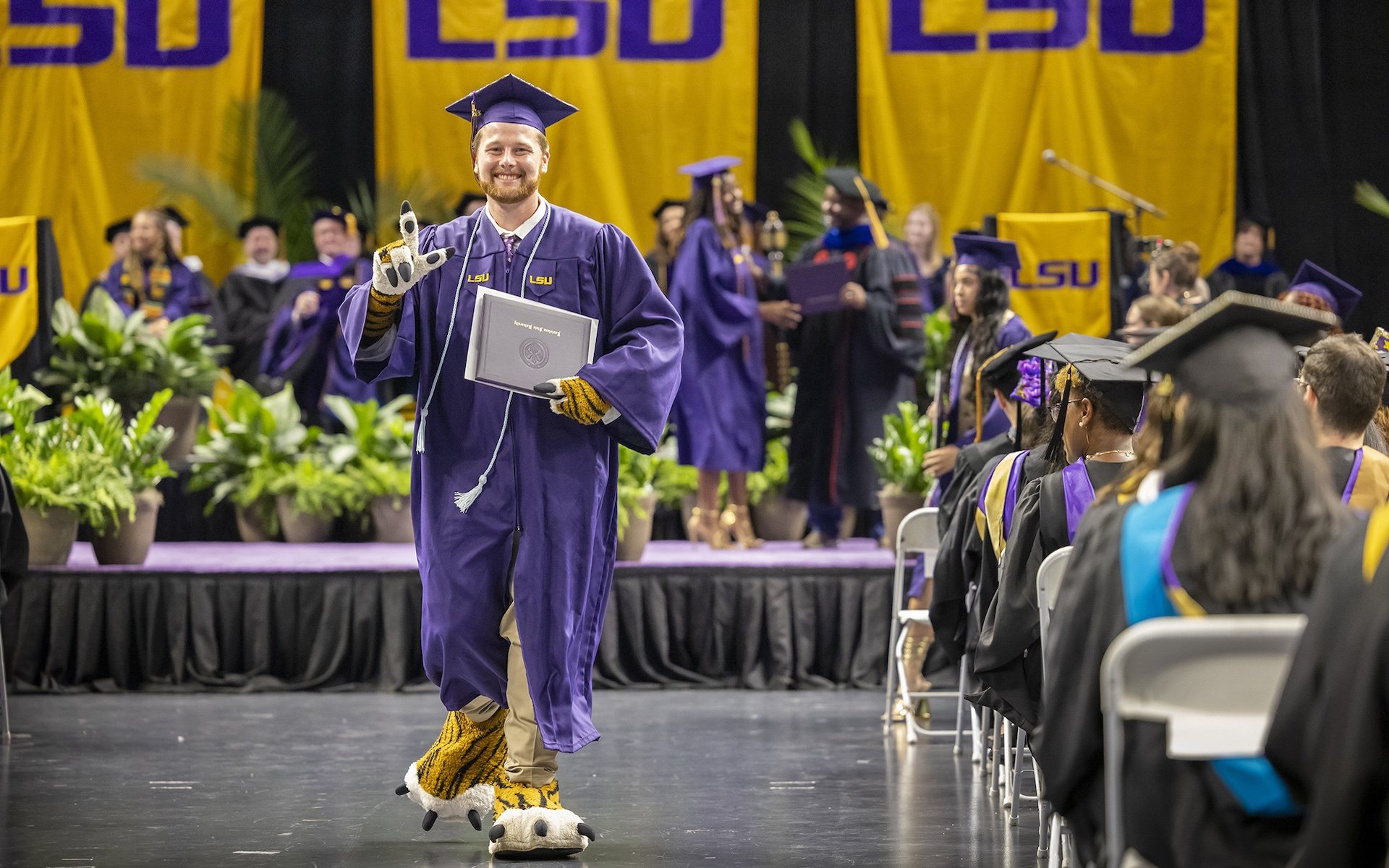 LSU grad in mascot gear walking at graduation ceremony