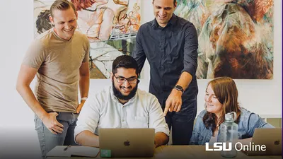 Four people are gathered around a laptop computer.