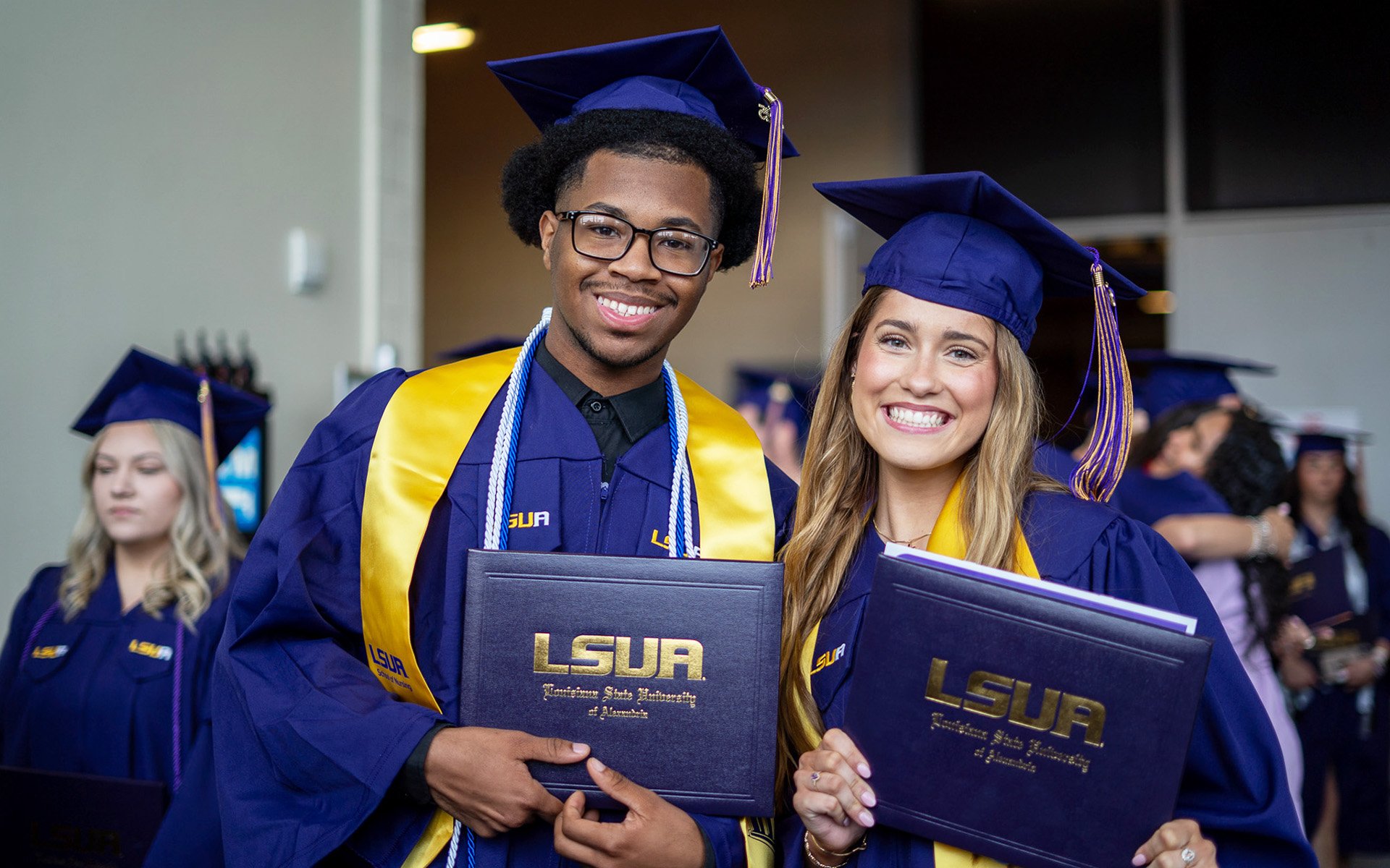 Two LSUA graduates smiling and holding their degree.