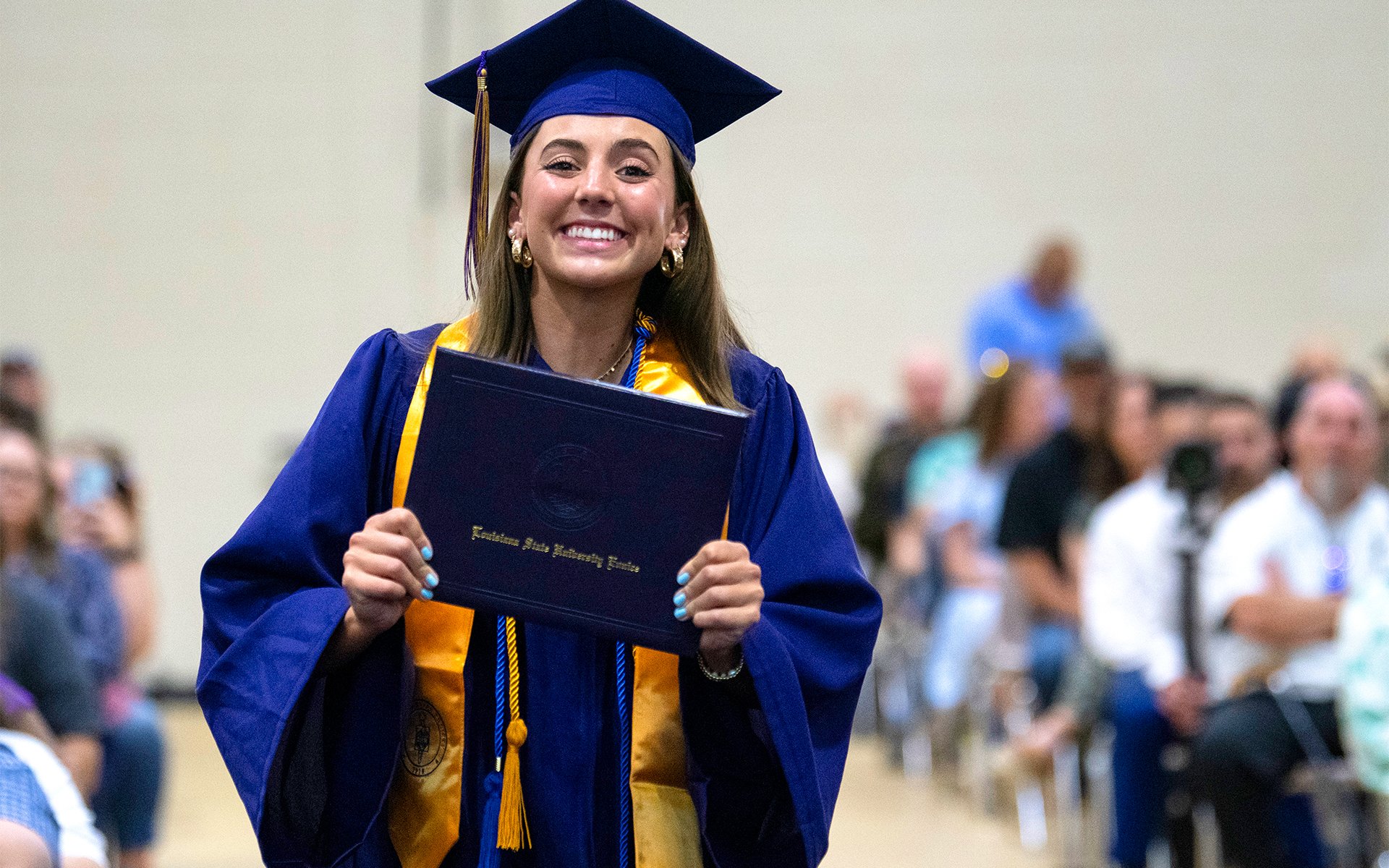 LSUE graduate holding degree and smiling at camera.