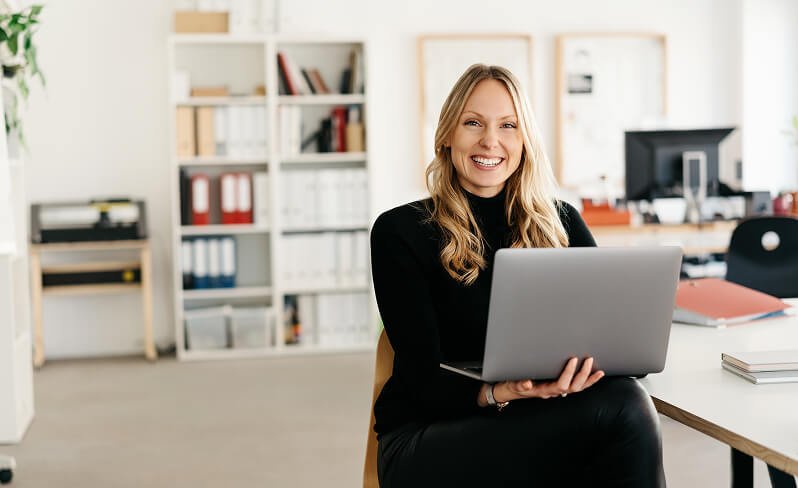 Woman sitting in chair holding laptop and smiling.
