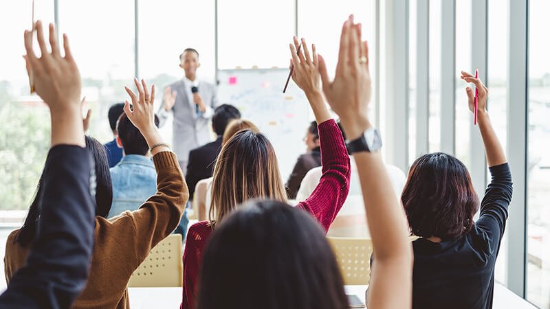 Room full of participants raising their hand to the speaker's question