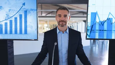 Man stands at podium in front of various charts and graphs.
