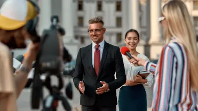 Campaign manager stands in background watching a political candidate do a media interview.