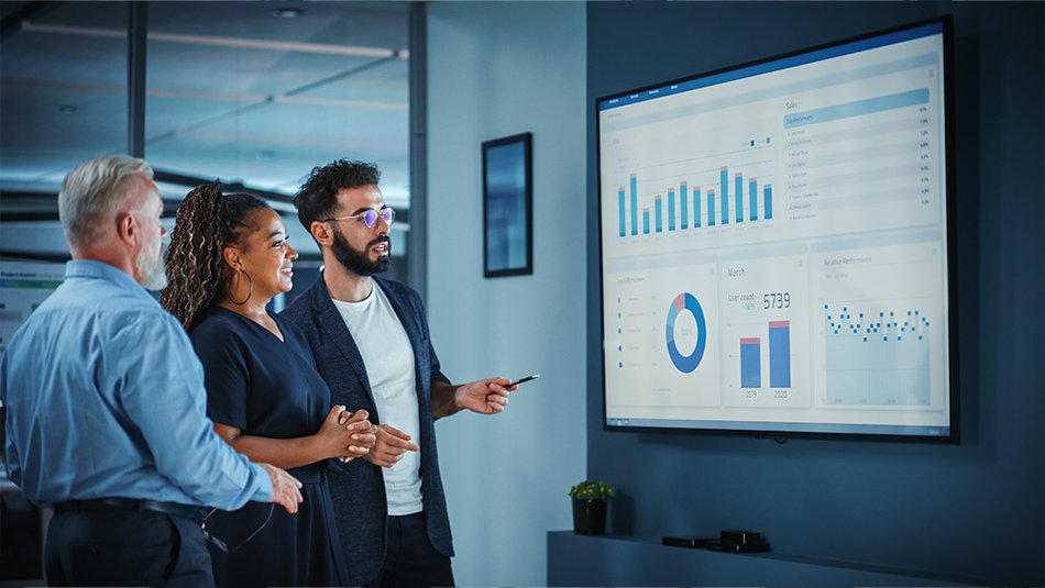 Two men and a woman looking at graphs and charts on a board