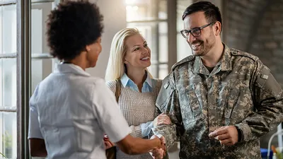 Military personnel shaking hands with a woman while smiling