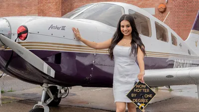 Tara Lauthe standing next to a plan with a graduation cap in her hand