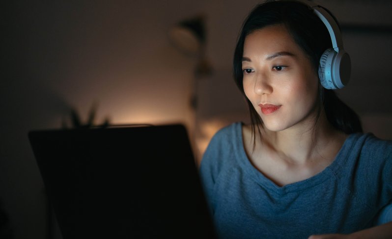 Female tech student working on laptop with headphones on.