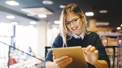 Teacher sitting at desk using tablet.