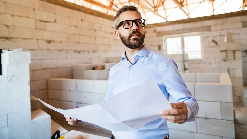 A construction manager holds a blueprint at a construction site.