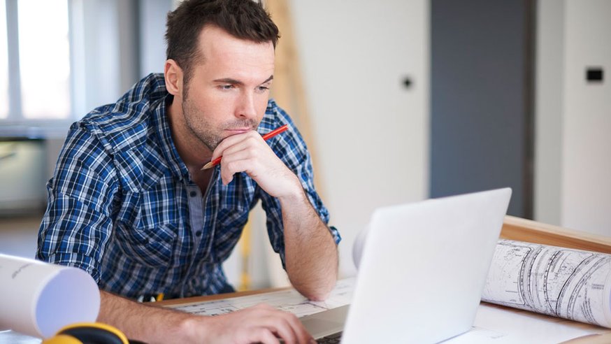 Man sits at desk reviewing blueprints.