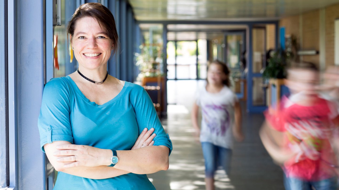Smiling educator standing in hall as students walk past