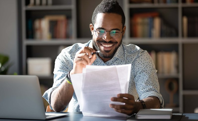 African American man looking at notes and studying in front of laptop